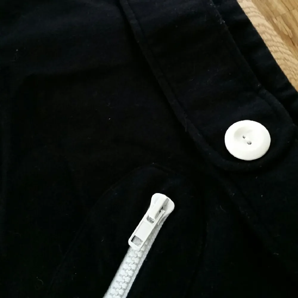 Svart kort kjol från H&M. Dragkedja baktill och dekorativa dragkedjor på framsidan samt dekorativt litet bälte framtill med två vita knappar. 
Använt skick.. Kjolar.