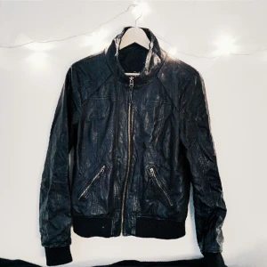  - Svart jacka i fuskskinn, ser dock äkta ut eftersom den inte är glansig som de ofta annars är. Superfint skick, som ny. Muddar nedtill och i ärmslut, tunnt foder och fickor med dragkedja. Jag har normalt stl 38.