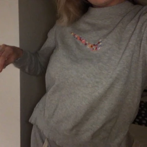 Grå sweatshirt broderat nike - En grå skön sweatshirt med broderat niketryck i form av små blommor. Storlek S men passar mig som har M, passar även XS. Tröjan har även små slitsar på sidan av tröjan. Startbud 250kr! Köparen står för frakt, kan mötas upp i Helsingborg. Hör av er om ni önskar beställa en egen tröja med broderat tryck! 