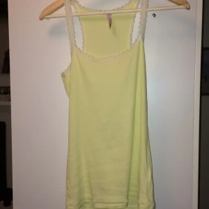  - Ribbat, blekgult linne från Fishbone. Spets kanter vid urringning, ärmar och rygg. Söt till svarta jeans. Något genomskinligt. Köparen betalar frakt!