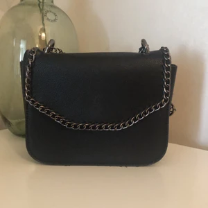 Svart Axel/Crossbody väska  - En snygg svart Axel/crossbody väska med kedjedetaljer. Den är i mycket bra skick då den bara är använd 2 gånger. Köpare står för frakt.