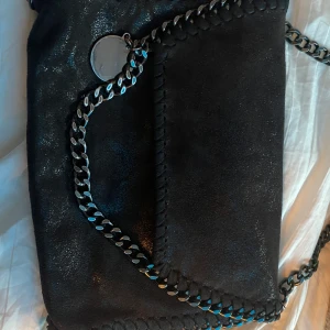 Väska  - En väska som är använd ett fåtal gånger. Svart med lite glittrigt tyg och och kedja som band. Inuti är det ett leopard mönster som även syns på bilden 