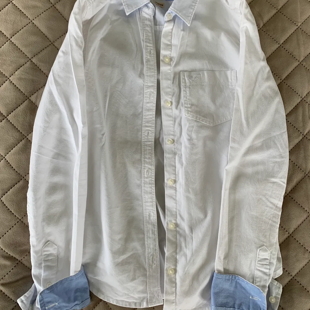 Säljer denna vita skjorta från Hollister med ljusblå detaljer! Aldrig använd! Pris: 100 kr (nypris 500 kr). FRAKT TILLKOMMER💗🧚🏼. Skjortor.