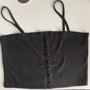 Svart ribbat linne med knappat - Svart ribbat linne med knappar, crop top stil, råkade köpa L men kunde inte lämna tillbaka, fri frakt✨