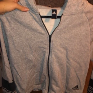 Adidas luvtröja. - Grå adidas tröja i kortare modell. Mjuk vaddering. Funkar som träningströja eller bara ha i vardagen. Då den varit för kort för mig har den knappt används! 
