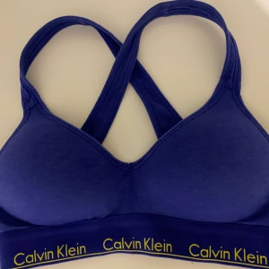 Calvin klein BH - En fin mörkblå Calvin Klein bh med gul text och korsade band. Även lite pushup. Den är endast använd några få gånger och nypriset är 550kr. 