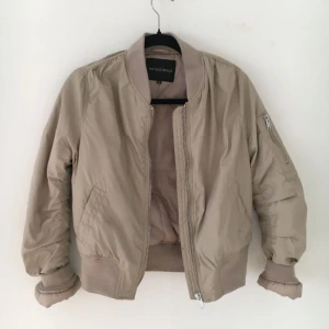  - Sandfärgad/beige bomberjacka från NA-KD med silvriga detaljer, använd 2-3 gånger. Lite stor i storleken så kan passa en S beroende på hur man vill att den ska sitta. Supersnygg och lite varmare än en vanlig bomber!
