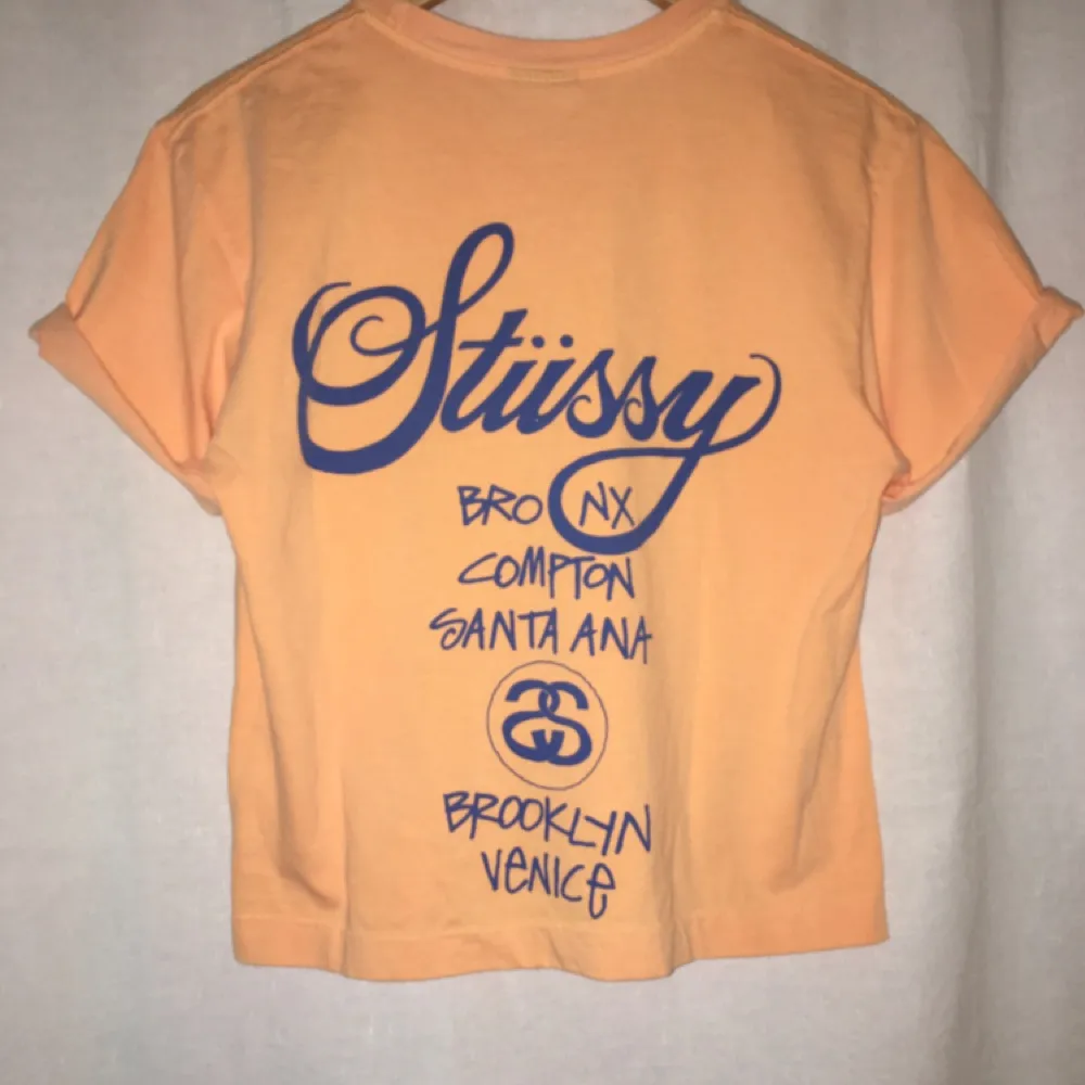 Snygg  persikofärgad Stüssy tröja med blå text + logga. Tröjan är uppsydd. . T-shirts.