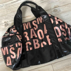  - En snygg väska med bokstäver som motiv i rosa, har två fickor på utsidan som man kan se på tredje bilden. Har även en ficka på insidan. 