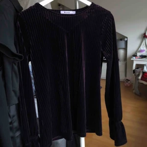  - Lila, långärmad topp i sammet/velvet från NAKD i storlek S. Randig i strukturen med glans och lyster. ALDRIG använd & är i NYTT skick!