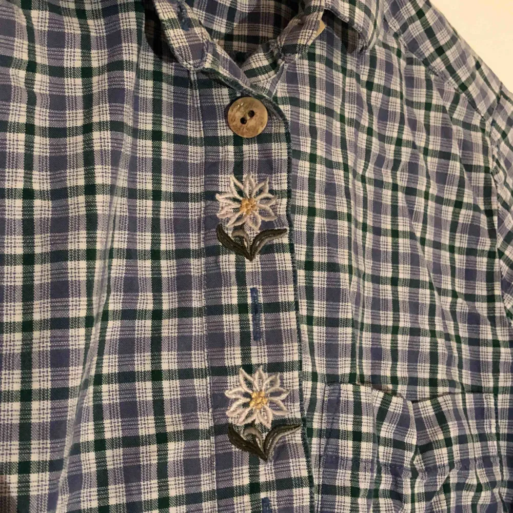 En rutig skjorta i blå, grön och vit med broderade blommor uppe i kragen och knappar i trä. Inga lösa lösa trådar eller knappar som saknas som jag kan se. (Inte inklusive frakt, det står köparen för!). Skjortor.