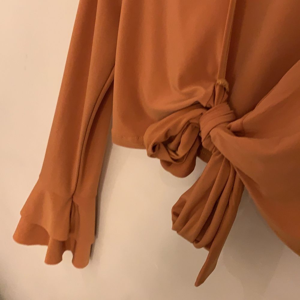 En orange/kopparfärgad blus i silke från boohoo. Knytning där fram och vida armar med volang. strl 38, aldrig använd så i nyskick.. Toppar.