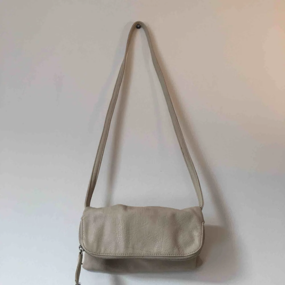En liten beige väska ( liknande kuvertväska ). Aldrig använd men lite sliten i dragkedjan.. Väskor.