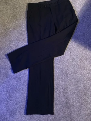 Svarta kostymbyxor med raka ben - Snygga svarta kostymbyxor med raka ben och diskreta fickor. Byxorna har bälteshällor och stängs med knapp och dragkedja. Materialet ser ut att vara en tunnare, vävd kvalitet som ger en stilren look. Perfekta till en dressad outfit.