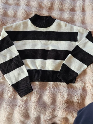 Svartvit randig stickad tröja - Snygg stickad tröja med breda svarta och vita ränder. Tröjan har en lite mer croppad passform, ribbade muddar och turtle neck. Materialet är mjukt och tröjan är väldigt gosig. 