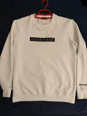Vit sweatshirt från Hugo Boss - Snygg vit sweatshirt från Hugo Boss med svart logotyp på bröstet och mindre logga på ärmen. Tröjan har rund halsringning, ribbade muddar och är tillverkad i mjukt material som känns skönt mot huden. Perfekt för en clean och stilren look.Köpt för 350 euro i Tyskland ungefär 1 år sedan.