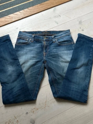 Blå jeans från Nudie Jeans Co - Säljer ett par klassiska blå jeans från Nudie Jeans Co med snygg slitning och raka ben. Jeansen har fem fickor, orangea sömmar och är gjorda i slitstark denim. Perfekta för dig som gillar en avslappnad och tidlös stil. Är aldrig använda säljer då de var för små. Modell - Lean Dean. Skriv vid minsta fundering pris går att diskuteras😃