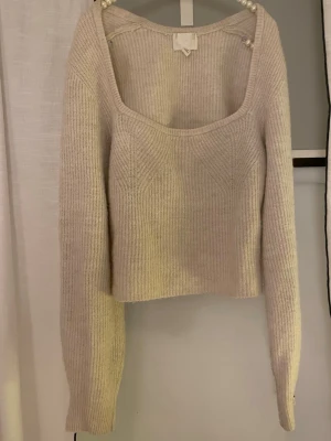 Ljusbeige stickad tröja med uringning - Säljer en ljusbeige stickad tröja med fyrkantig halsringning och långa ärmar. Tröjan har ribbstickad struktur och är lite kortare i modellen, perfekt för att matcha med jeans. Materialet är mjukt och mysigt! 