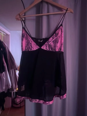 Svart och rosa loungewear-linne - Säljer ett snyggt loungewear-linne med tunna axelband. Toppen har svarta och rosa partier med mönster upptill och nedtill. Luftig och bekväm passform.