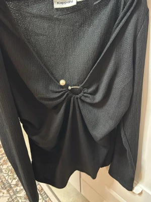 Svart v-ringad topp från Kappahl - Stilren svart topp från Kappahl med v-ringning och dekorativ pärldetalj framtill. Toppen har lång ärm och är tillverkad i ett ribbat material som ger en snygg struktur. Perfekt att matcha med både jeans och kjol.