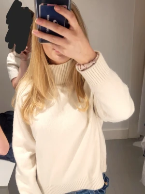 Vit stickad polotröja - Säljer en stilren vit stickad polotröja med ribbade muddar och hög krage. Tröjan har en avslappnad passform och är perfekt att matcha med jeans för en clean look. Materialet känns mjukt och skönt mot huden.