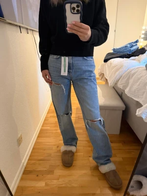 Ljusblåa ripped jeans med raka ben - Säljer ett par ljusblåa jeans med raka ben och slitningar på knäna. Jeansen har klassisk femficksdesign och hög midja. Perfekt för dig som gillar en avslappnad och trendig look. Materialet är denim och de har en cool vintage vibe.