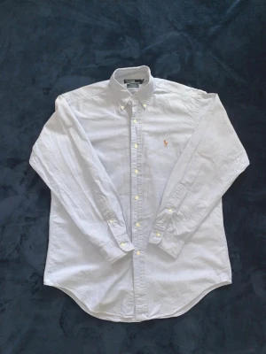 Vit skjorta från Ralph Lauren - Klassisk ljusblå skjorta från Ralph Lauren med broderad logga på bröstet. Skjortan har lång ärm, knappar hela vägen och button-down krage. Tillverkad i bomull och har en tidlös, clean look som passar till många stilar. 10/10 skick till ett dunder pris.