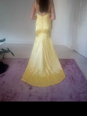 Gul långklänning i satin - Elegant gul långklänning i glansigt satinmaterial med smala axelband och figurnära passform. Klänningen har en vacker siluett och knäppning i ryggen, perfekt för speciella tillfällen. Helt ny och oanvänd. Inköpt från USA! Pris kan diskuteras 