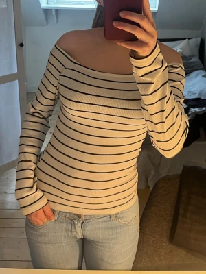 Randig offshoulder topp i ribbad bomull - Snygg offshoulder topp med svarta ränder på vit botten. Ribbad och figurnära modell med långa ärmar, perfekt för en trendig look.Sydde in tröjan själv för en tajtare passform. Men den är skön och stretchig, och därmed inte jobbigt att ha på sig. 