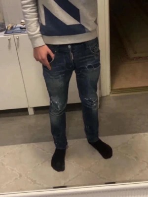 Blå Dsquared2 jeans med slitningar - SIZE 42 i Dsquared2 STORLEK, Säljer ett par blå jeans från Dsquared2 med snygga slitningar och detaljer på benen. Jeansen har slim passform och klassisk femficksdesign. Märkeslapp bak i midjan. Perfekta för dig som gillar streetstyle. Små tecken på användning men allmänt väldigt bra skick