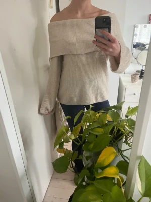 Beige off shoulder stickad tröja - Trendig beige stickad tröja med off shoulder-design och bred krage. Tröjan har långa ärmar och är ribbstickad för en snygg struktur. Perfekt för dig som vill ha en stilren och modern look.