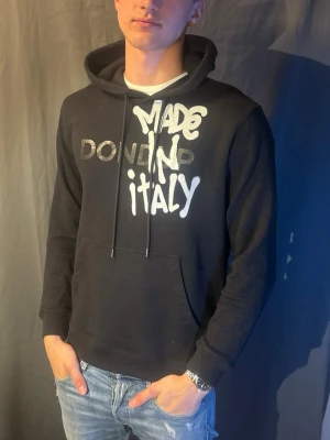 Svart hoodie Dondup Made in Italy - Cool svart hoodie från Dondup med vit och grå text 'Made in Italy' på bröstet. Klassisk huva med snören och stor magficka. Modellen är 190cm och väger 80kg. Skriv om du har frågor 🥰