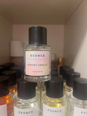 Aurora Vanille parfym från ESSNCE - Aurora Vanille från ESSNCE är en Eau de Parfum i en stilren, rund glasflaska med svart lock. Etiketten har en mjuk pastellfärg och flaskan rymmer en transparent vätska. Doften är framtagen av Margareta Grääs och har en tydlig vaniljkaraktär.