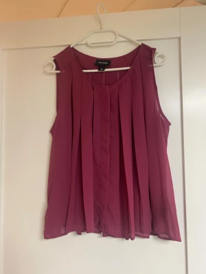 Plommonlila plisserad topp från monki  - Säljer en plommonlila ärmlös topp från monki med snygga plisserade detaljer. Toppen är luftig och har rund halsringning. Materialet är tunt och lätt, vilket ger ett flowy intryck. Perfekt att styla med jeans eller kjol för en trendig look.