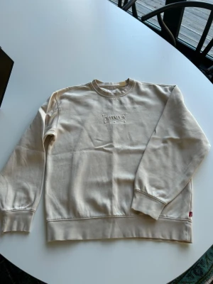Beige sweatshirt från Levi's  - Säljer en beige sweatshirt från Levi's med broderad logga på bröstet. Tröjan har rund halsringning, ribbade muddar vid ärmslut och nederkant samt en mjuk insida. Perfekt för en avslappnad och stilren look.
