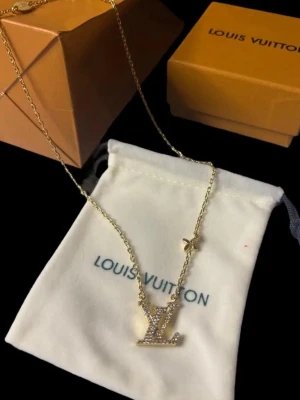 💛 Guldfärgat halsband Louis Vuitton - Snyggt guldfärgat halsband från Louis Vuitton med ett glittrande LV-hänge dekorerat med små stenar. Kedjan är tunn och har även en liten stjärndetalj. Perfekt för dig som gillar exklusiva accessoarer och vill sticka ut.
