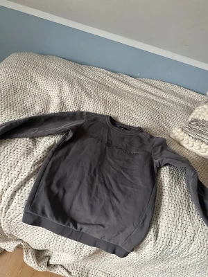 Mörkgrå crewneck från Sail Racing - Snygg mörkgrå sweatshirt från Sail Racing med diskret logga på bröstet. Klassisk rund halsringning och långa ärmar. Tillverkad i mjukt bomullsmaterial som känns skönt mot huden. Perfekt till jeans eller joggers. Passar upp till 16 år. 