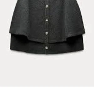 Svart ponchotröja med knappar - Mysig grå ponchotröja med knäppning framtill. Tröjan har en lös passform och ribbstickad kant vid hals och nederdel. Perfekt för lager-på-lager och enkel att styla till olika outfits.