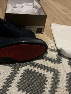 Svarta sneakers från Christian Louboutin - Snygga svarta sneakers från Christian Louboutin med den ikoniska röda sulan. Skorna har lågt skaft, är tillverkade i en mix av mocka och läder. Perfekta för dig som vill ha något exklusivt och stilrent. Skicka privat för bättre bilder