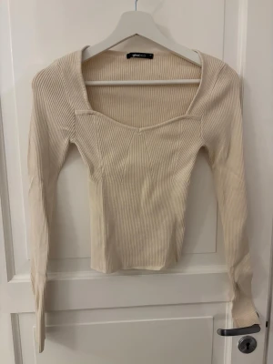 Ribbad beige topp från Gina Tricot - Trendig ribbad topp i beige från Gina Tricot med lång ärm och snygg fyrkantig ringning. Figurnära passform och stretchigt material som ger en modern look. Perfekt att styla med jeans eller kjol för en clean outfit.