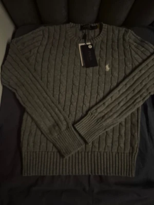Ralph Lauren - Säljer en snygg grå dam cable knit tröja från Ralph lauren | I färgen grå med vit logga och storlek S | Helt ny och fräsch | Hör av er för mer information/bilder! 