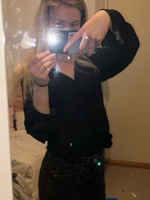 Svart blus med v-ringning - Säljer en svart blus med v-ringning och långa ärmar. Blusen har en enkel och stilren design som passar till många olika outfits. Materialet ser ut att vara lätt och mjukt, perfekt för att skapa en snygg look.