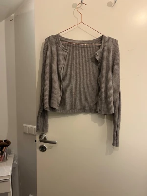 Grå ribbad kofta med knappar - Säljer en grå ribbstickad kofta med långa ärmar och knäppning framtill. Den är knappt använd koftan har inga hål eller skador.