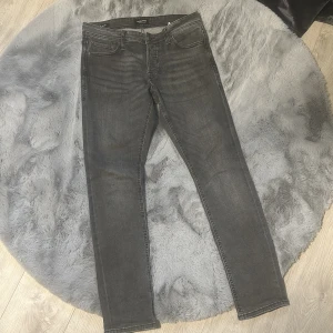 Grå slim fit jeans från Jack & Jones - Snygga grå slim fit jeans från Jack & Jones med klassisk femficksmodell och dragkedjegylf. Je ger en modern sopad look och är tillverkade i stretchigt denimtyg för extra komfort. Perfekta till en avslappnad streetstyle.