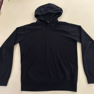 Svart hoodie med huva - En klassisk svart hoodie med huva och dragsko. Hoodien har långa ärmar och ribbade muddar vid ärmslut och nederkant. Perfekt för en avslappnad och stilren look.