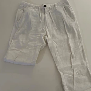 Vita linnebyxor  - Säljer ett par vita linnebyxor med avslappnad passform och dragsko i midjan. Byxorna har snedställda fickor fram och en knappstängning. Perfekta för en chill och stilren look.