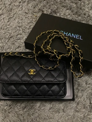 Svart Chanel quiltad handväska - Säljer en klassisk svart quiltad handväska från Chanel i läder med guldfärgad kedja och ikoniska CC-loggan framtill. Väskan har elegant rutmönster och kommer i originalbox. Perfekt för dig som vill ha en tidlös och lyxig accessoar.