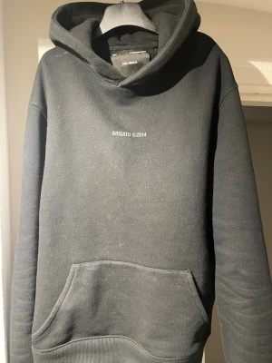 Svart hoodie från Axel Arigato - Svart hoodie från Axel Arigato med trycket 'ARIGATO ©2014' på bröstet och i större format på ryggen. Klassisk känguruficka framtill, ribbade muddar och huva. Perfekt för en clean och stilren streetwear-look. Är en å 170 och den är lite för liten 