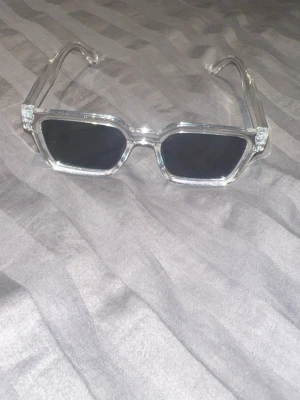 Transparenta solglasögon med klar båge - Säljer ett par trendiga solglasögon med transparenta bågar och rundad form. Glasen är också klara vilket ger ett stilrent och modernt uttryck. Perfekt för dig som vill ha en clean look och gillar minimalistiska accessoarer.