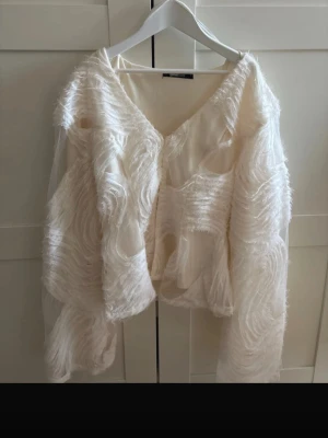 Vit fluffig blus från Gina Tricot - Unik vit blus från Gina Tricot med transparenta partier och fluffiga, vågiga detaljer över hela plagget. Blusen har v-ringning och långa ärmar i mesh-tyg som ger ett luftigt och trendigt intryck. Perfekt för dig som vill sticka ut med en statement piece. Priset går att diskutera❤️❤️